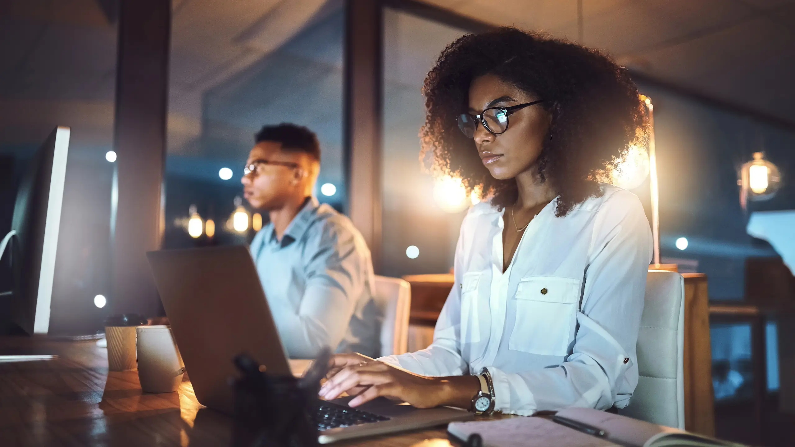 A marketer working with her colleague, collaborates on a laptop in a brightened room. They smile at each other.