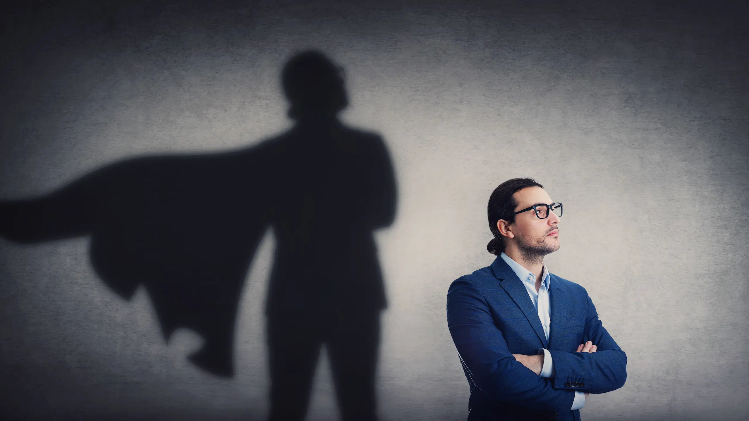 Confident businessman looking determined as casting a powerful superhero shadow on the wall. Motivated and ambitious business person shows inner strength.